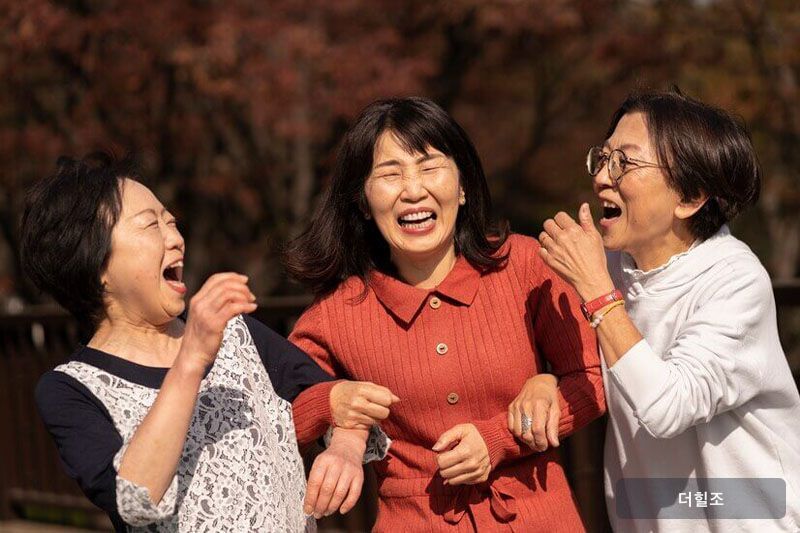 야외에서 서로 마주 보며 활짝 웃는 중년 여성 세 명